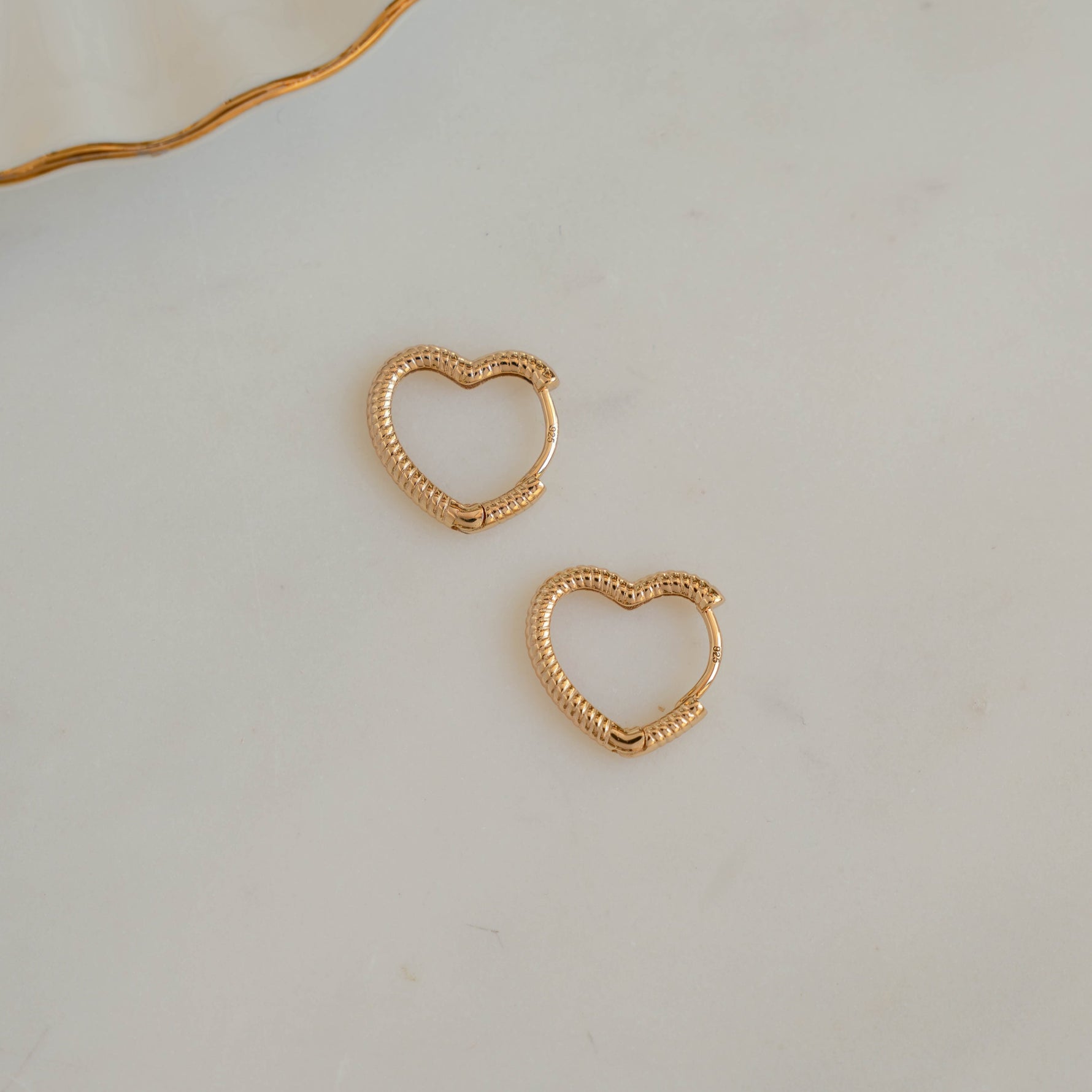 Dainty gold earrings with heart design, gift for her, shown on white marble background