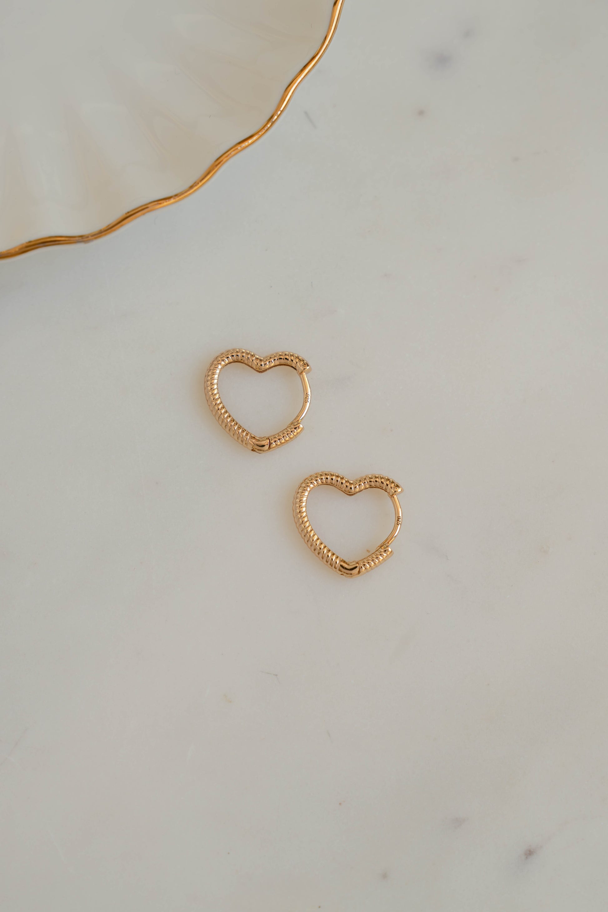 Dainty gold earrings with heart design, gift for her, shown on white marble background