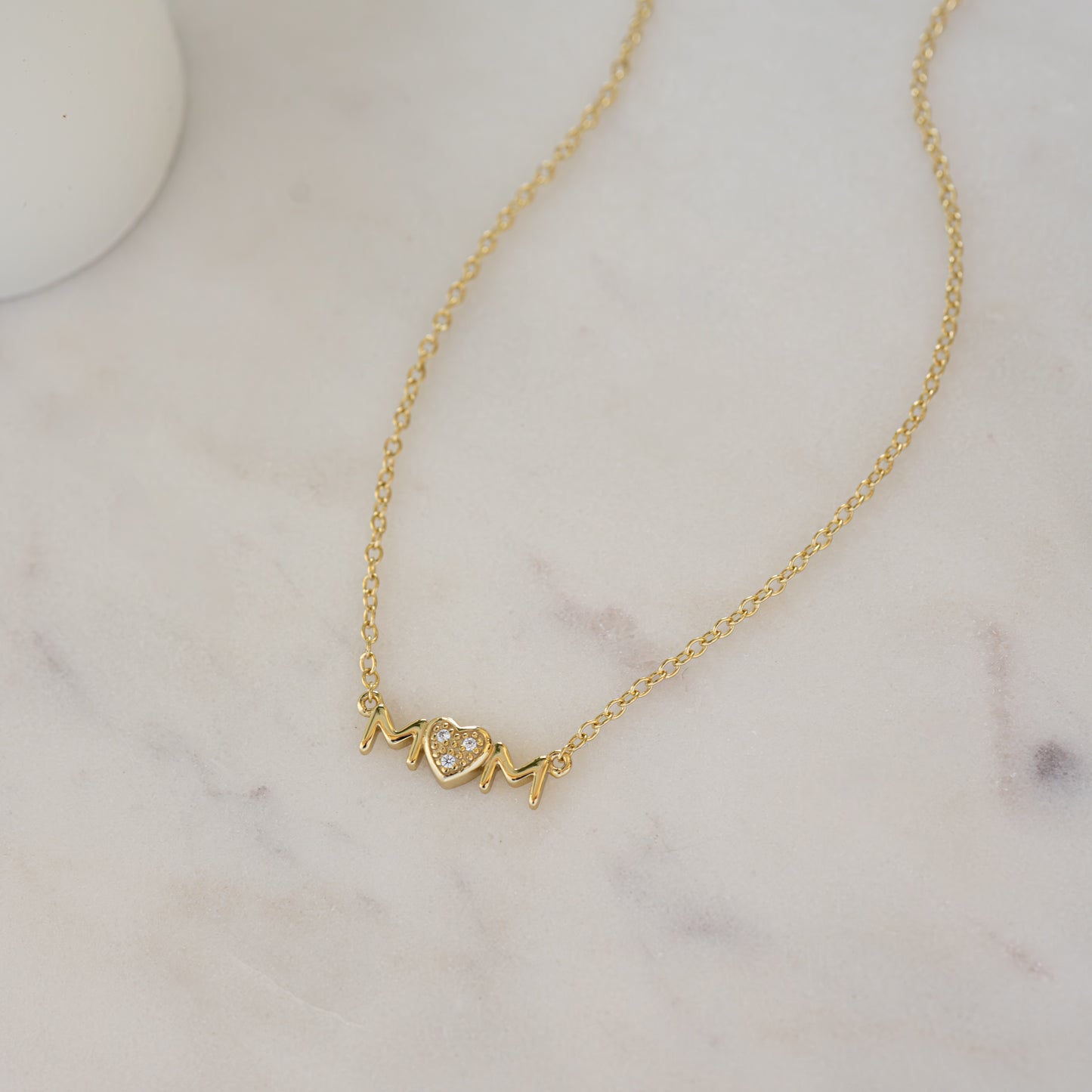 Close-up of a gold "MOM" necklace with a CZ heart, perfect for a Mother’s Day gift.