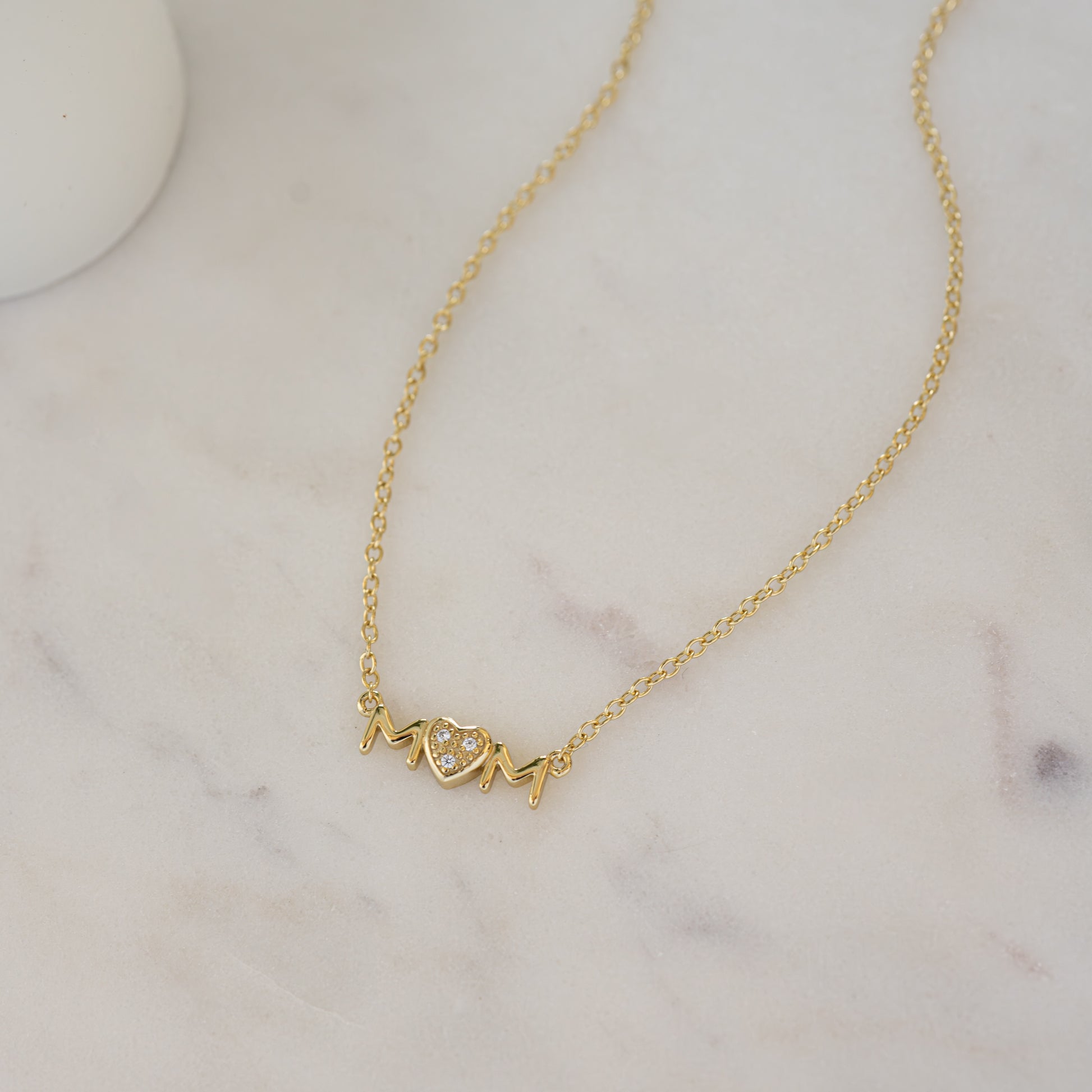 Close-up of a gold "MOM" necklace with a CZ heart, perfect for a Mother’s Day gift.