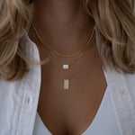 Chic halo emerald cut pendant necklace on Cuban link chain layered on model, cubic zirconia stone, layered with gold chain necklaces and dainty personalized dog tag necklace for her.