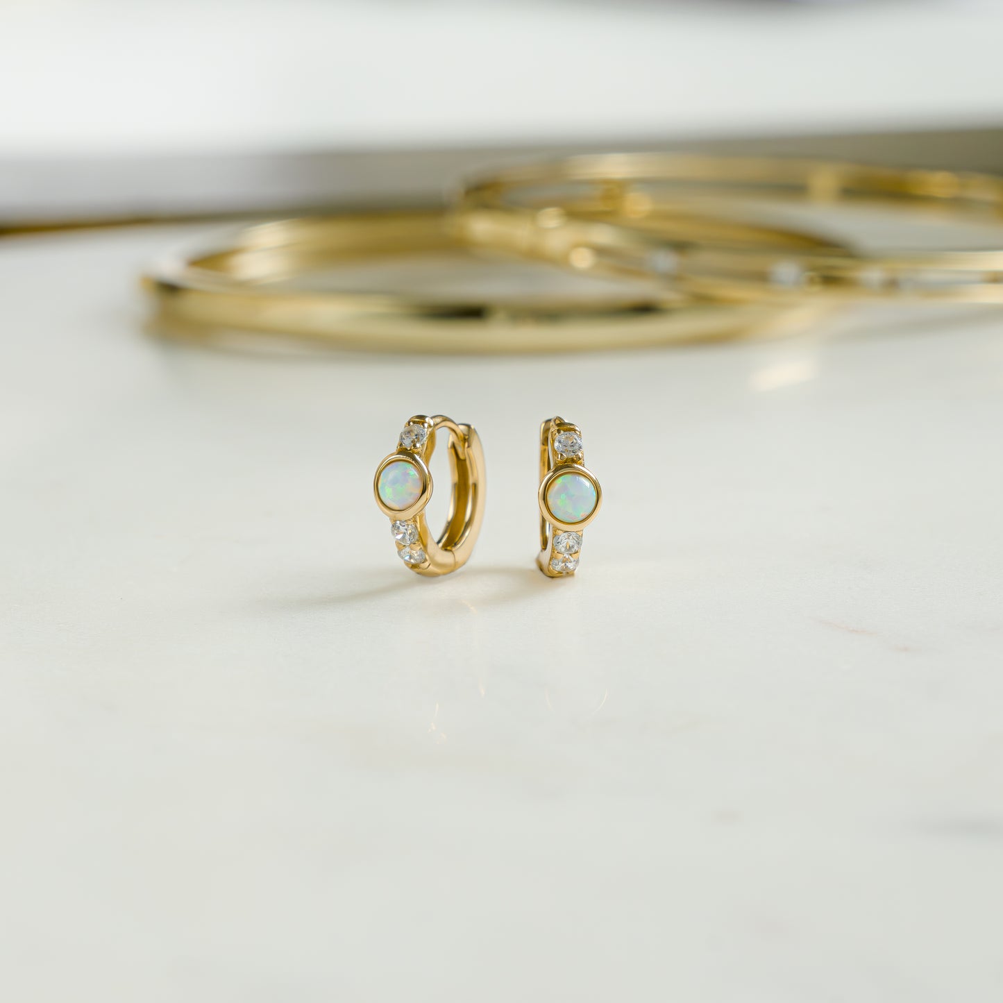 Close up image of gold studded cz opal earrings. The dainty opal earrings feature cz diamonds with a solitaire opal stone. 