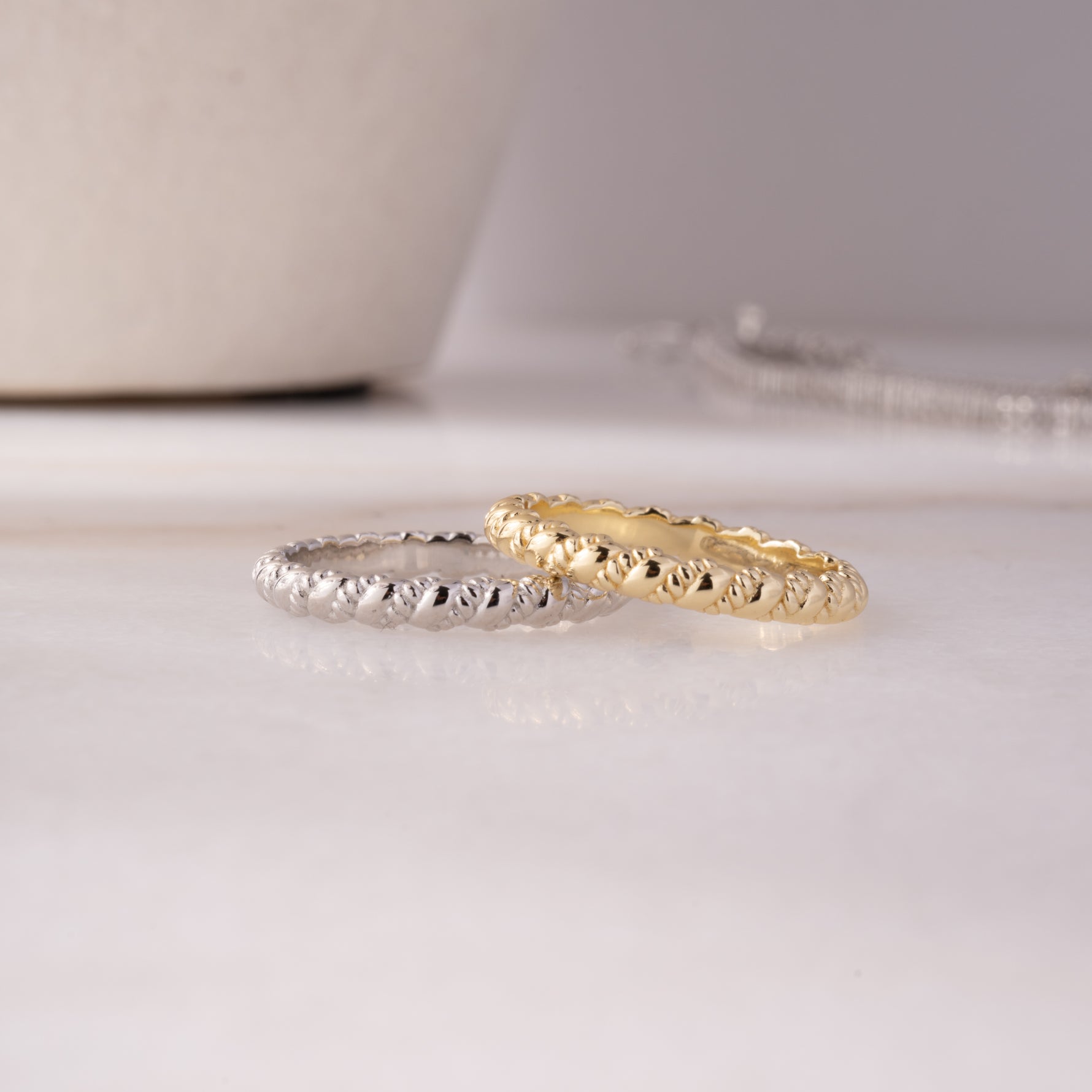 Minimalist stacking rings, one gold and one sterling silver, flat laid on a marble top,  highlighting their intricate yet dainty twisted design.