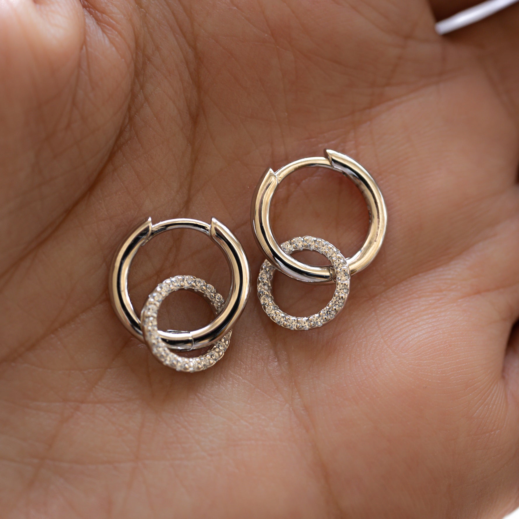 Close-up of shimmering pavé circle charm, gently dangling from a smooth, silver hoops, held on palm. 