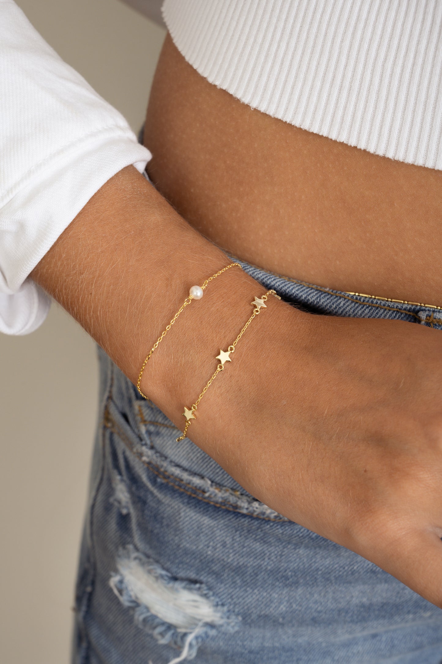model wearing a dainty pearl bracelet and a minimalist star charm bracelet