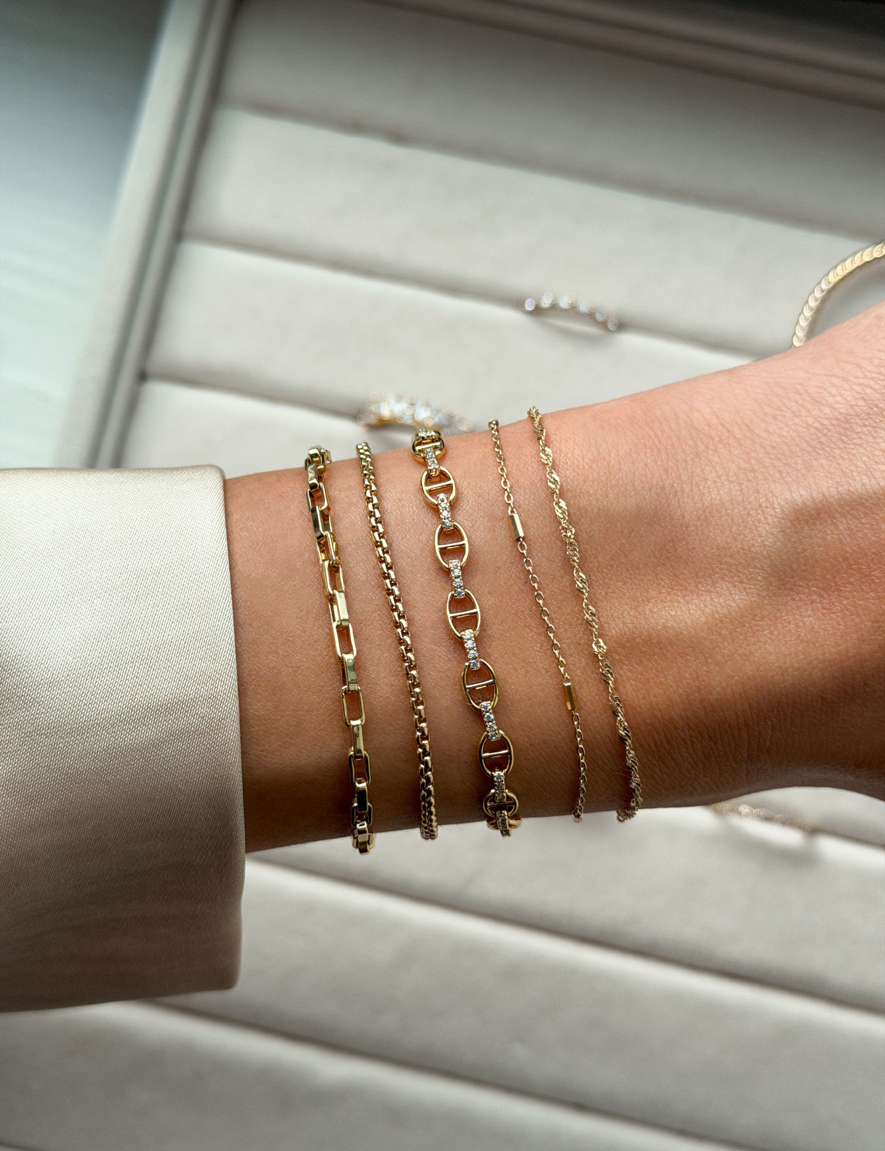 Close-up of a wrist wearing multiple gold chain bracelets on a neutral background