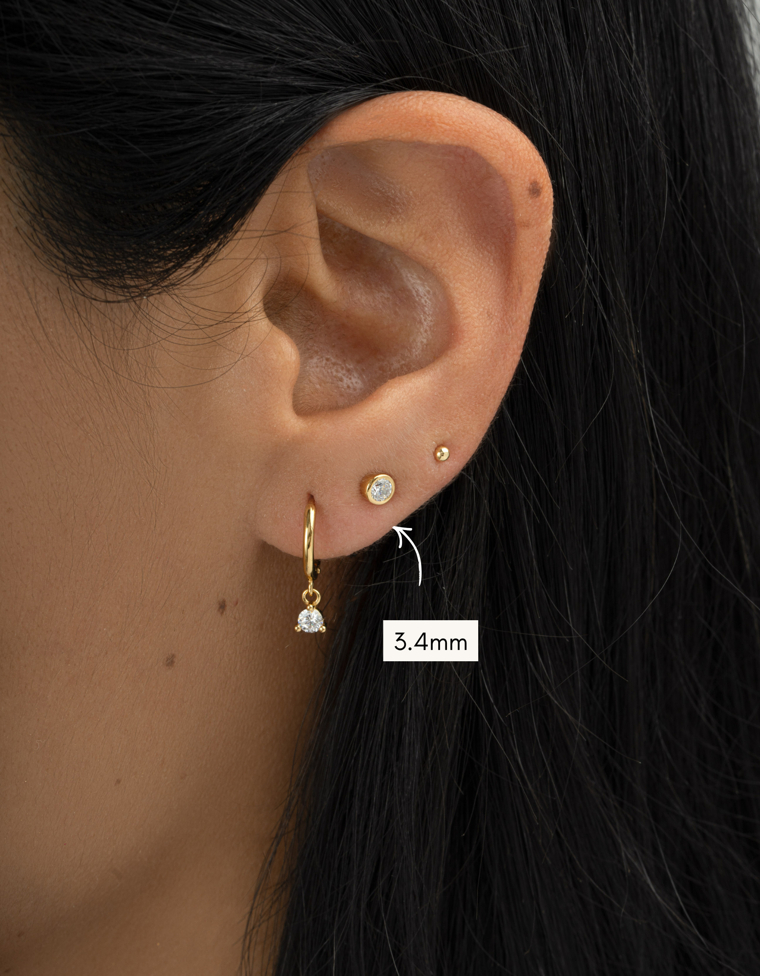 Close-up of an ear wearing gold earrings with a size label indicating 3.4mm.