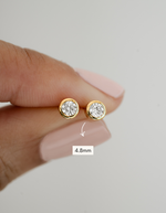 Gold stud earrings with diamond-like stones held between fingers, size indicated as 4.8mm.