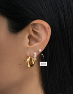 Gold hoop earrings with embedded stones worn by a person, close-up of ear.