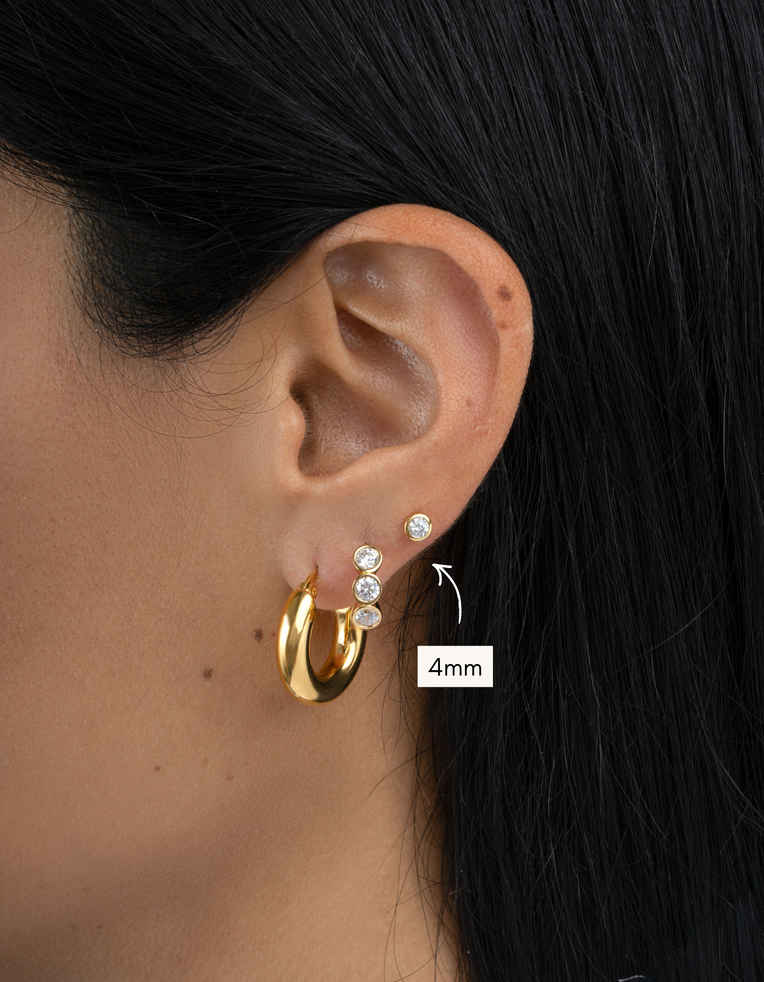 Gold hoop earrings with embedded stones worn by a person, close-up of ear.