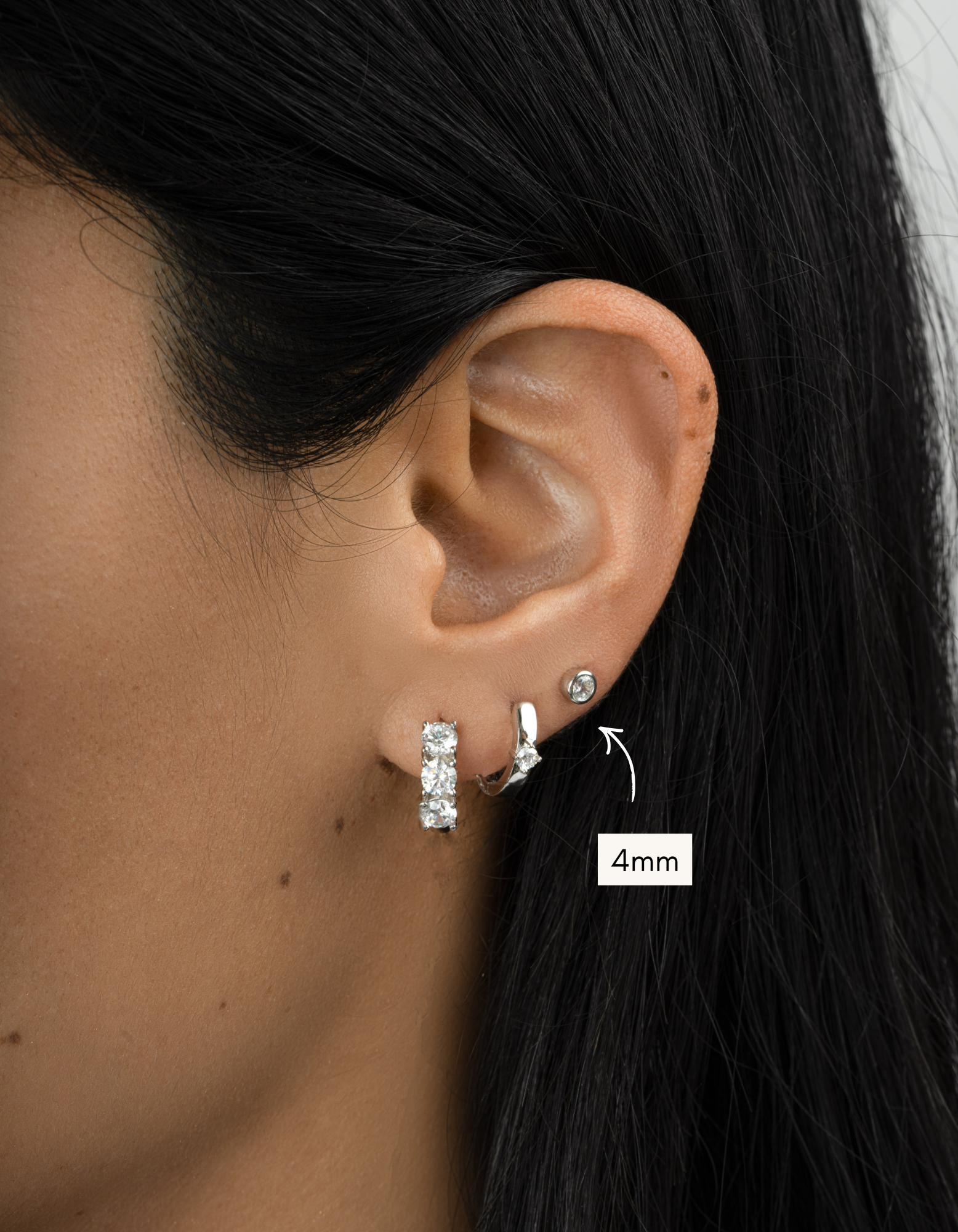 Close-up of an ear wearing two silver earrings with a size label indicating 4mm.