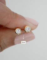 Gold earrings with clear gemstones held between fingers, size indicated as 5mm.