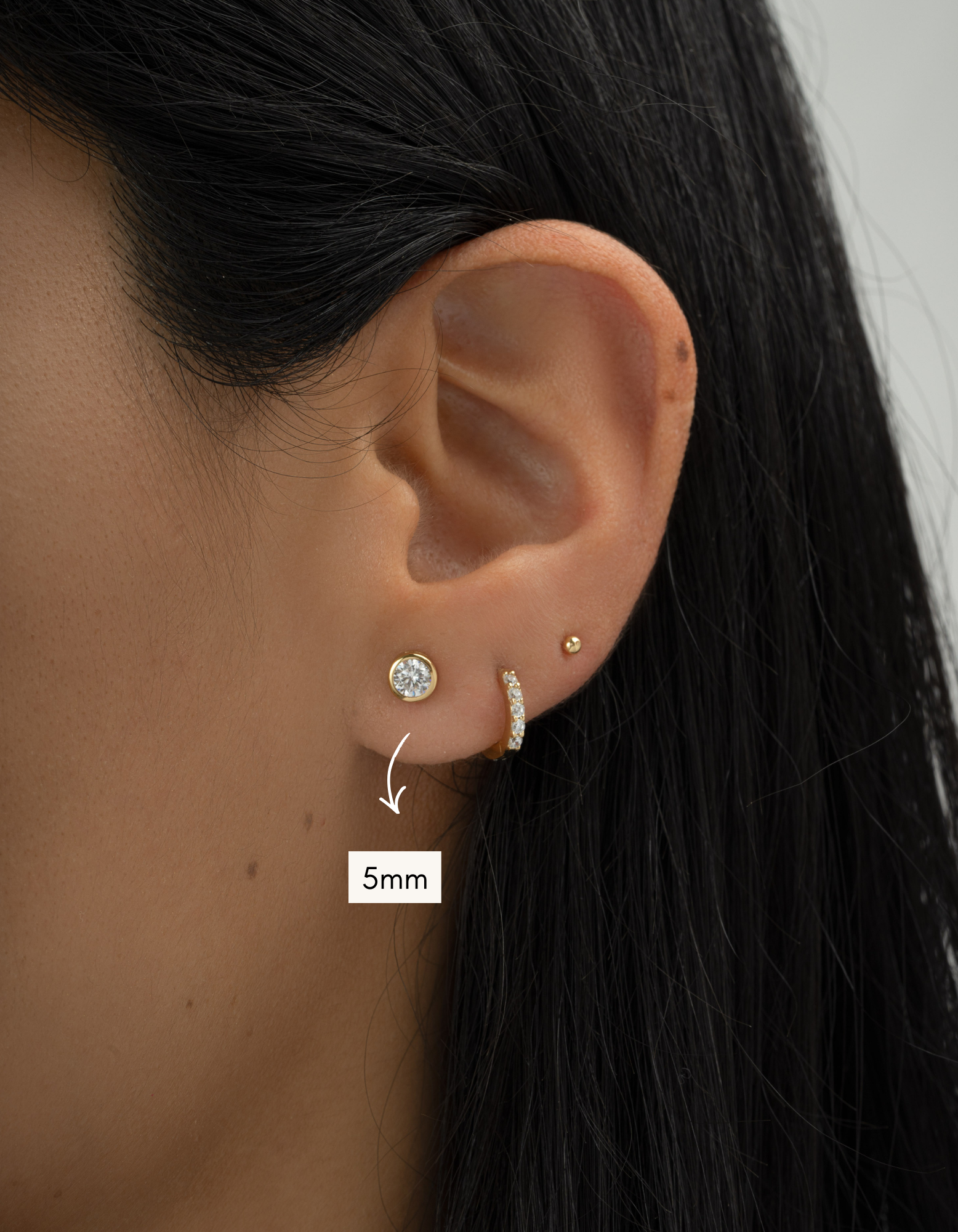 Close-up of an ear wearing two earrings with a size label indicating 5mm.