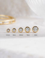 Bezel gold stud earrings with varying diamond sizes on a light background