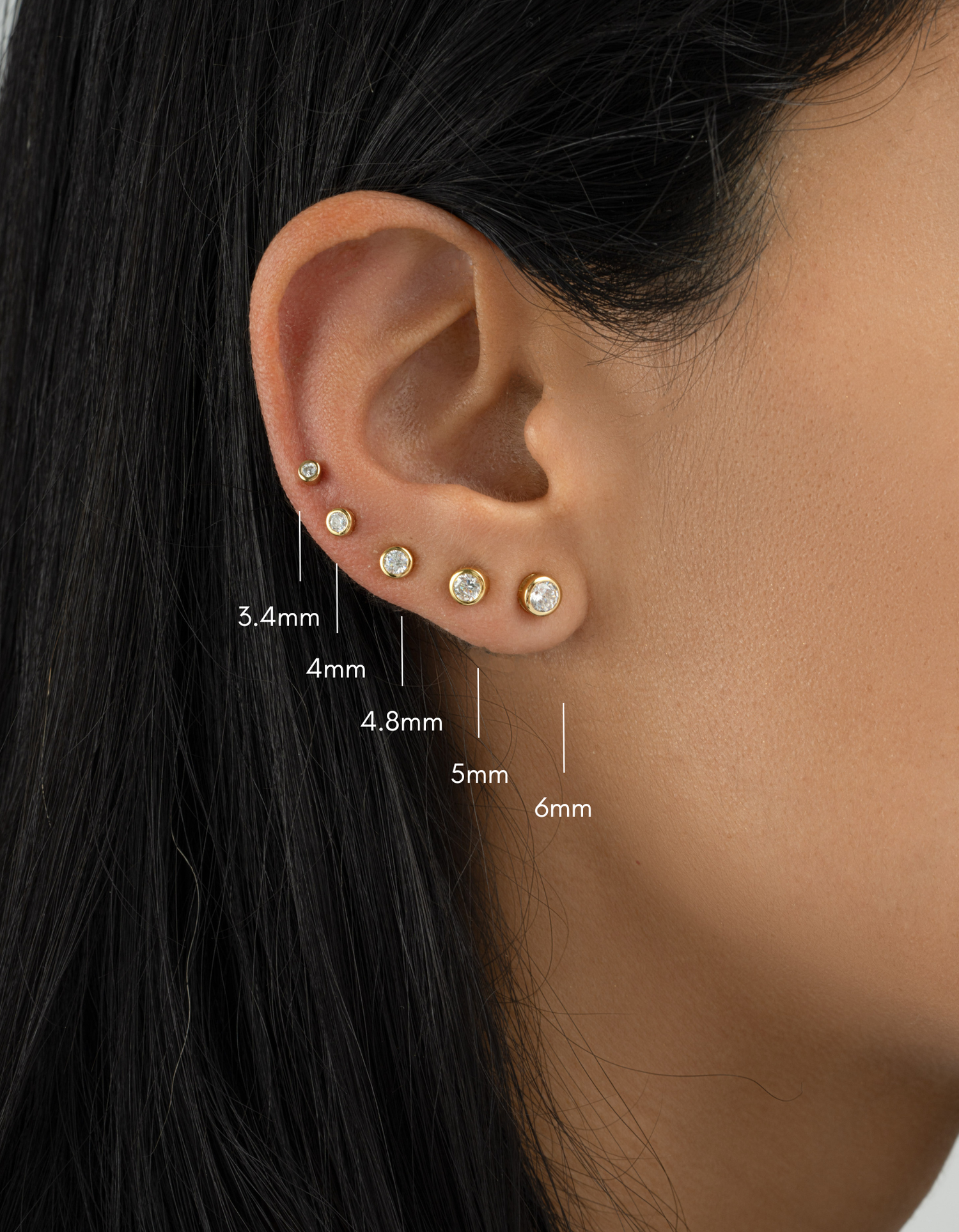 Close-up of an ear with gold earrings and size measurements indicated.