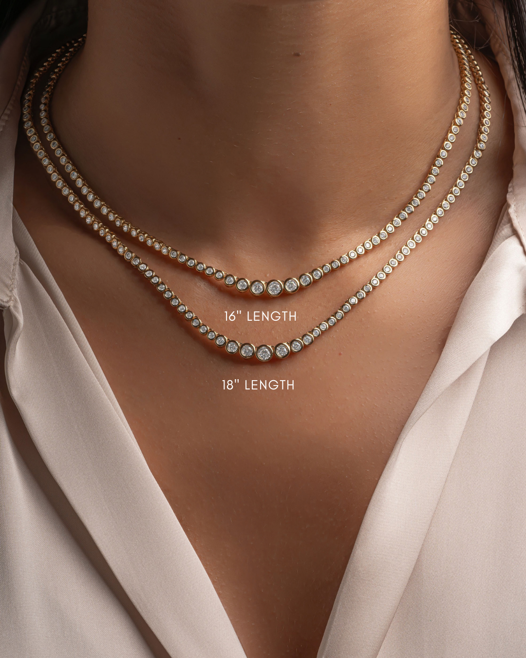 Close-up of a model wearing two layered gold necklaces with cz stones, one labeled 16" length and the other 18" length, against a white satin shirt.