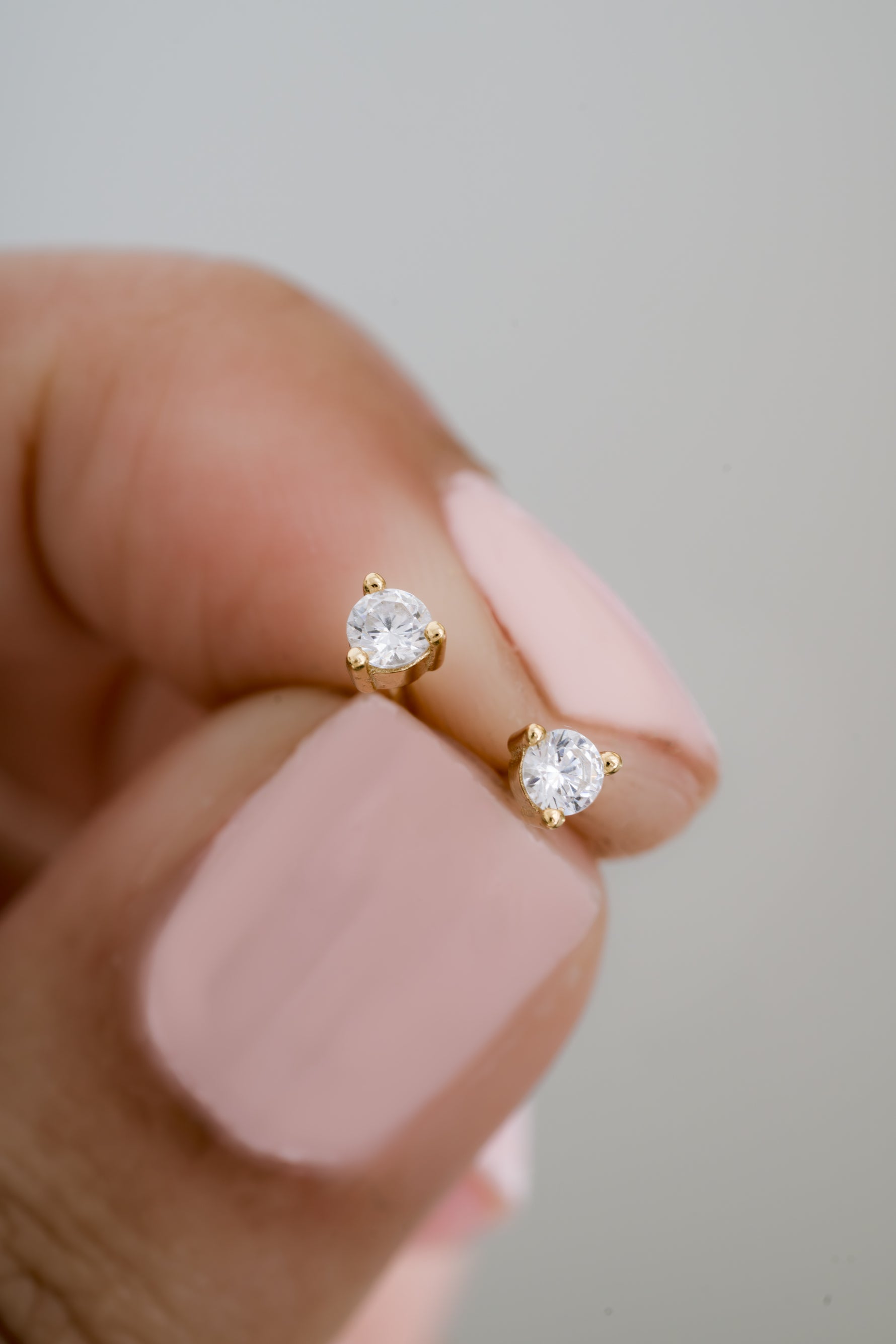 gold diamond solitaire stud earrings in between fingers