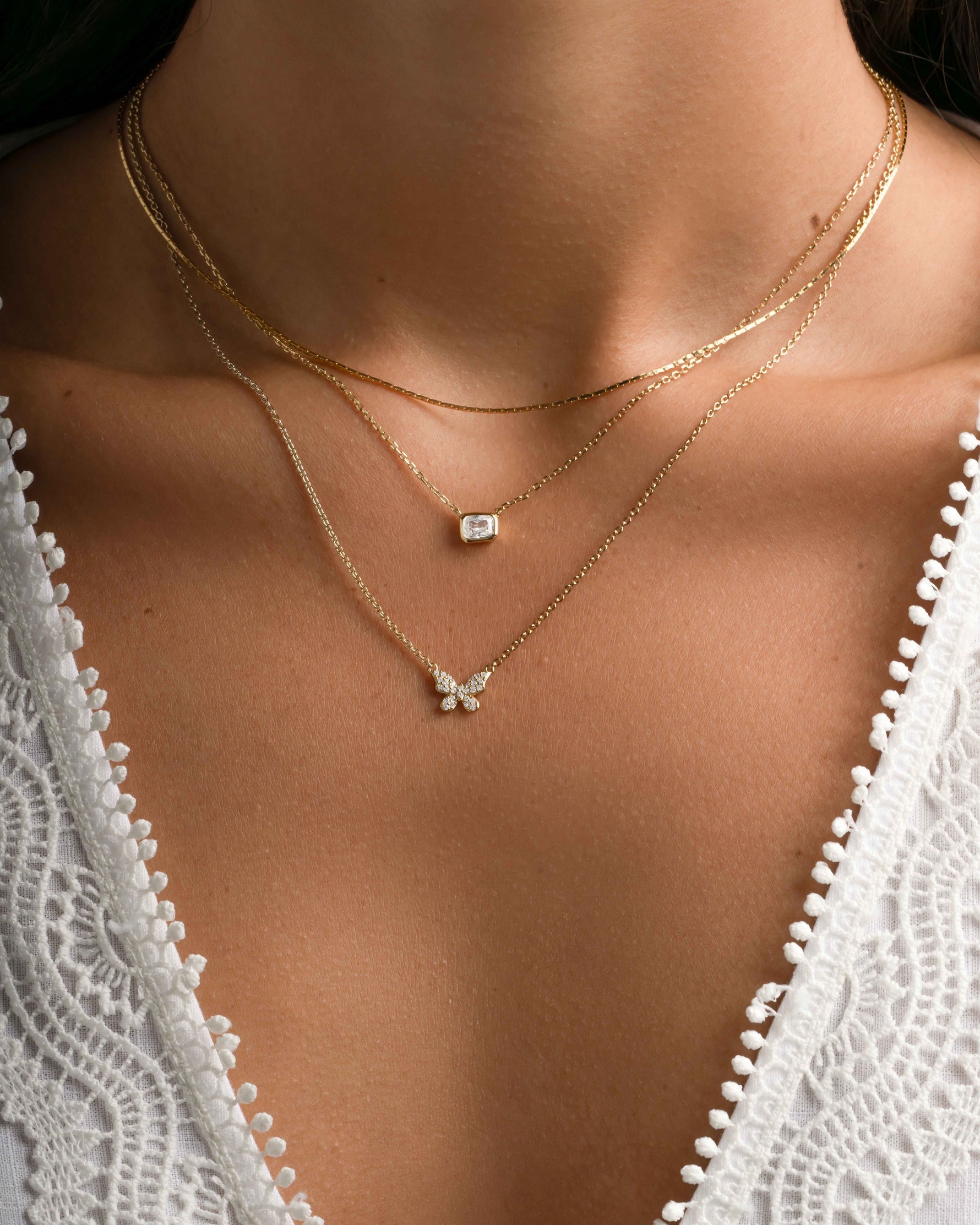 Gold butterfly necklace by Sami Jewels featuring diamond accents, styled on a model with layered necklaces.