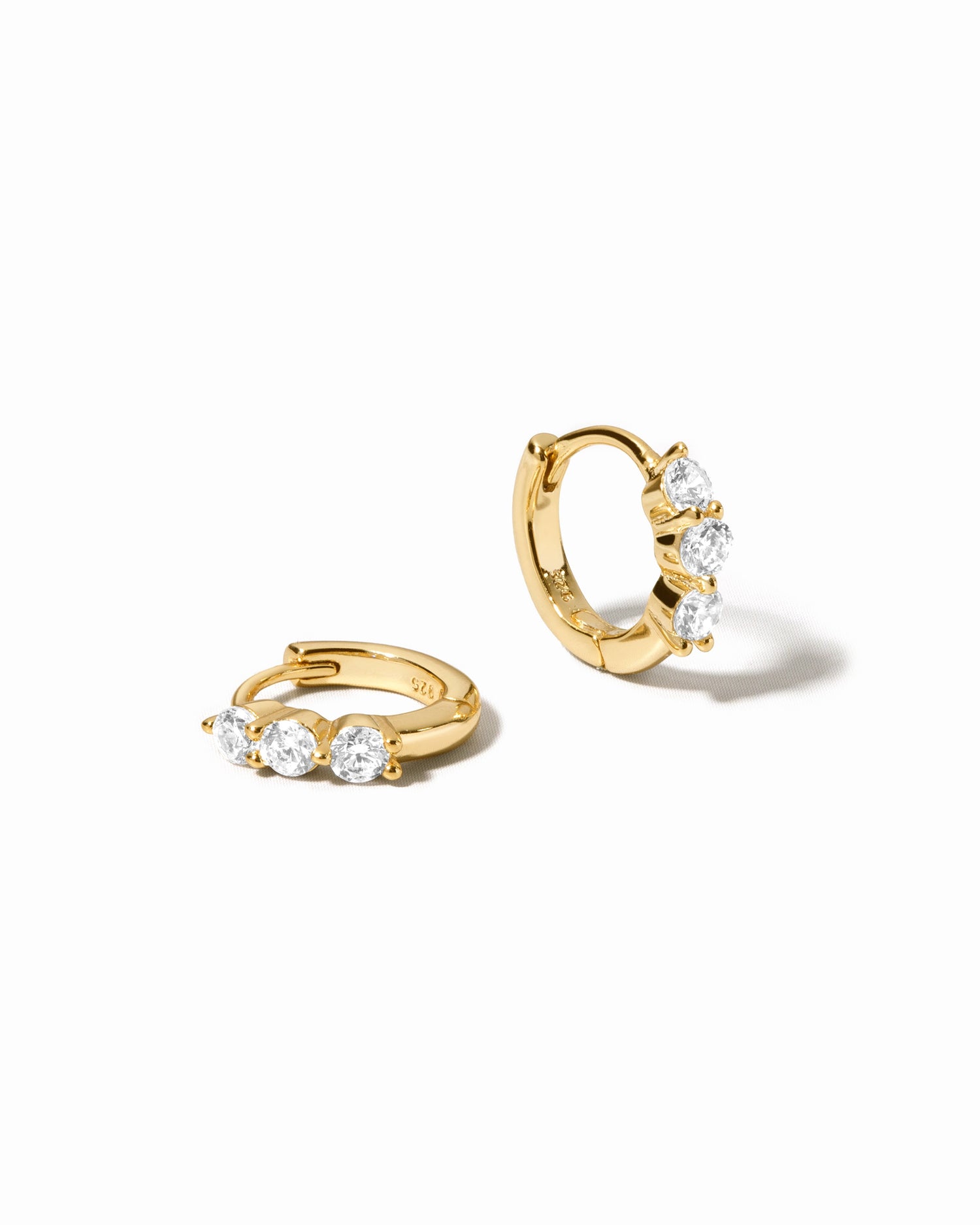 three stone diamond huggie hoop earring in gold on a white background