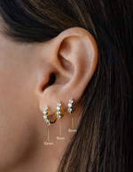 diamond huggie hoop earrings in different sizes, 10mm, 9mm, and 8mm in gold on a models ear