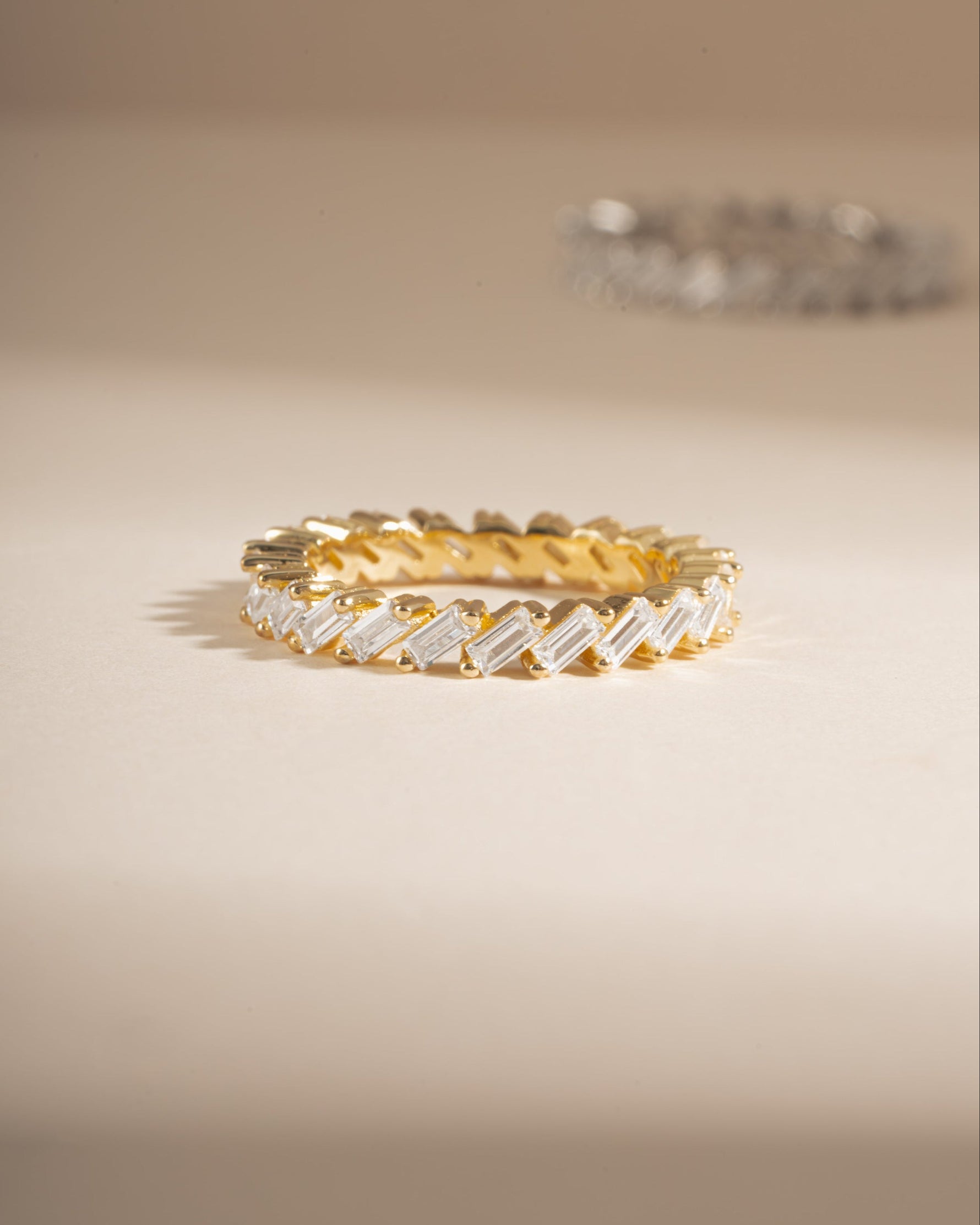 Slanted white cubic zirconia baguette ring in gold, showing the ring's design and sparkling stones on a white background.