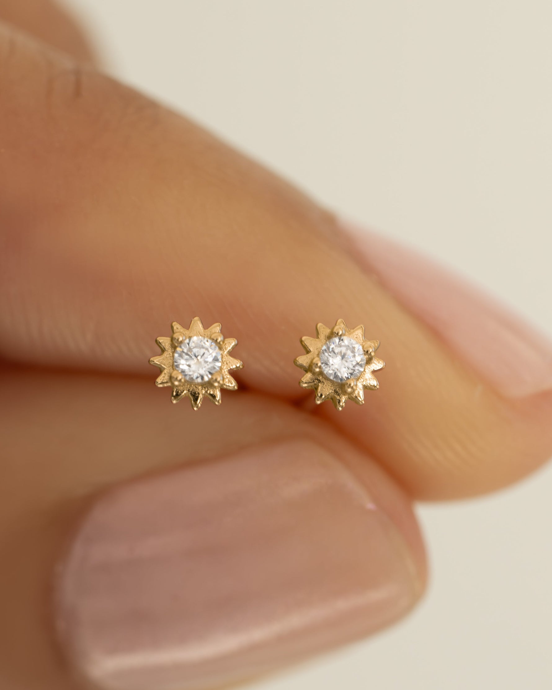 Close-up of CZ Tiny Sunburst Stud Earrings by Sami Jewels, featuring sparkling diamond-like sunburst design in silver-tone metal.
