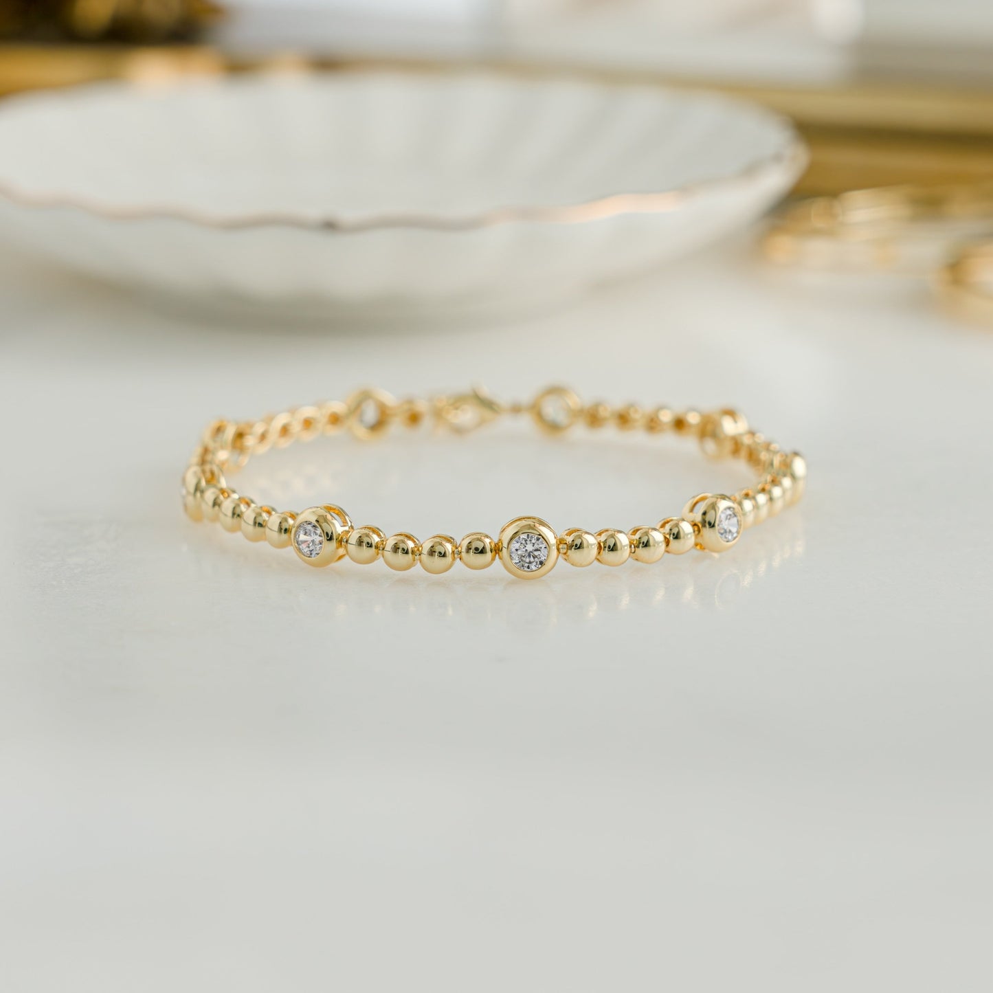 Gold tennis bracelet with small beads and large bezels.