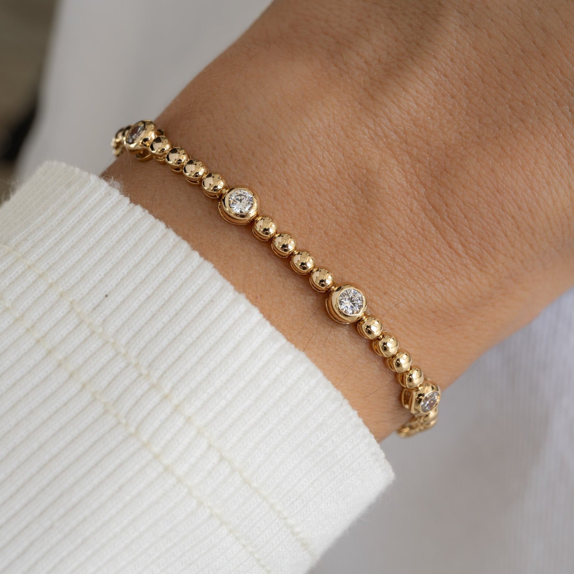 Model wearing a gold bezel tennis bracelet with large and small diamond accents.