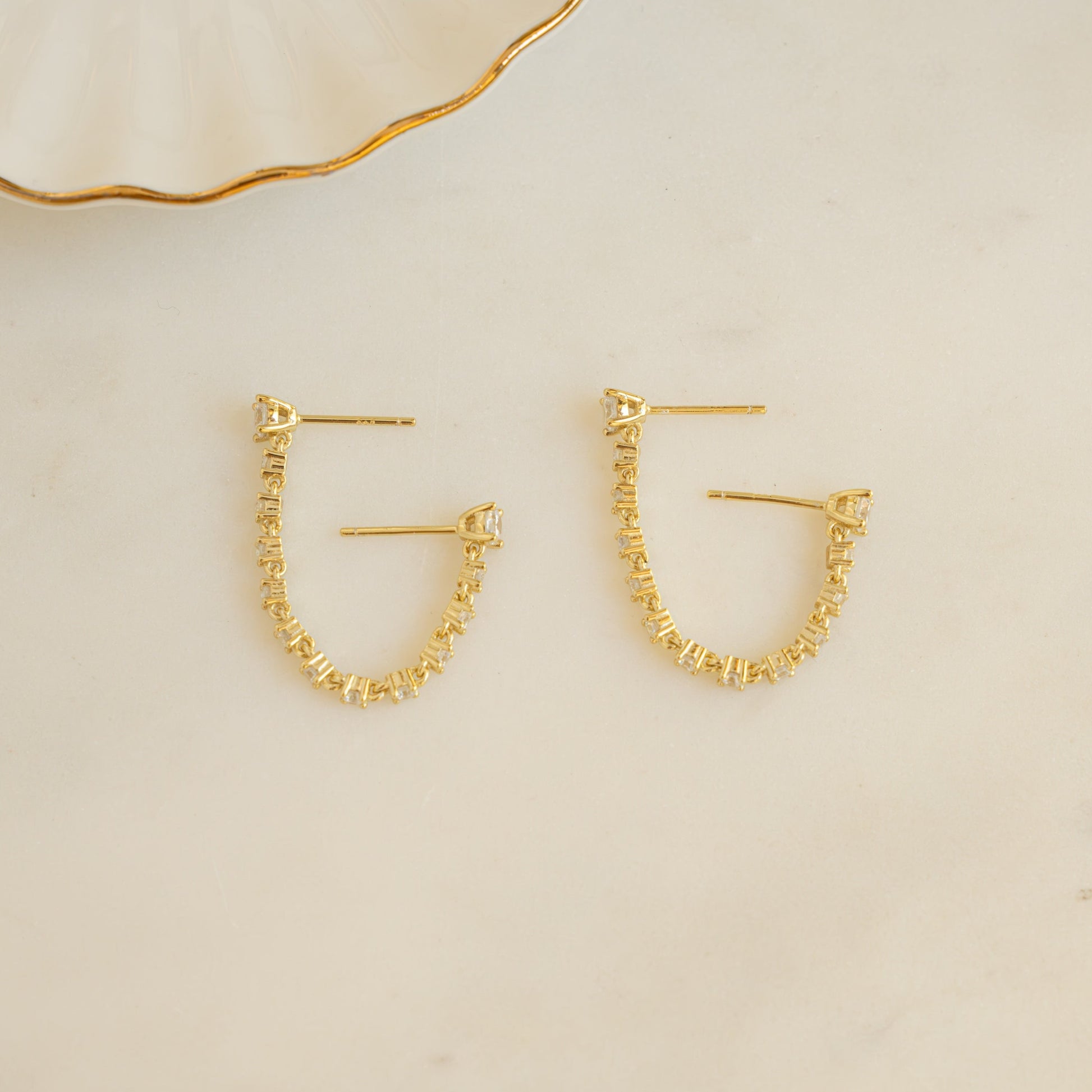 flat lay of gold stud earrings connected by a delicate tennis chain.