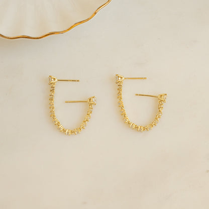 flat lay of gold stud earrings connected by a delicate tennis chain.