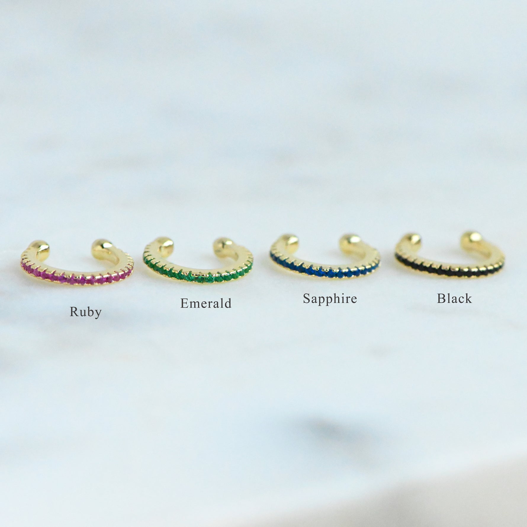 ear cuffs on a simple background in ruby, emerald, sapphire, and black