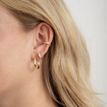 model wearing a curated ear with a small gold hoop, a diamond huggie earring and a gold ear cuff on her cartilage