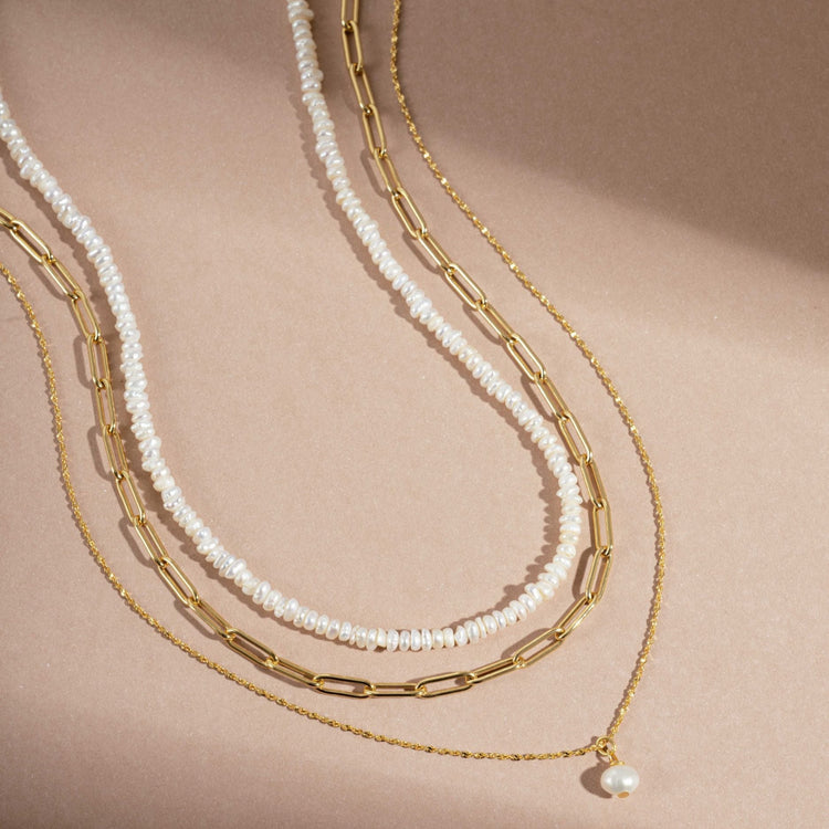 Two gold necklaces with pearl accents on a beige background