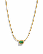 Gold necklace featuring emerald baguette bezel setting, statement jewelry piece with a sleek design on a white background.