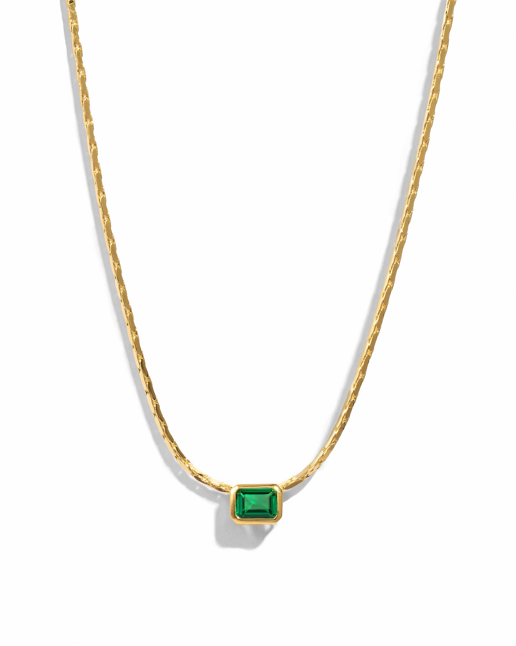 Gold necklace featuring emerald baguette bezel setting, statement jewelry piece with a sleek design on a white background.