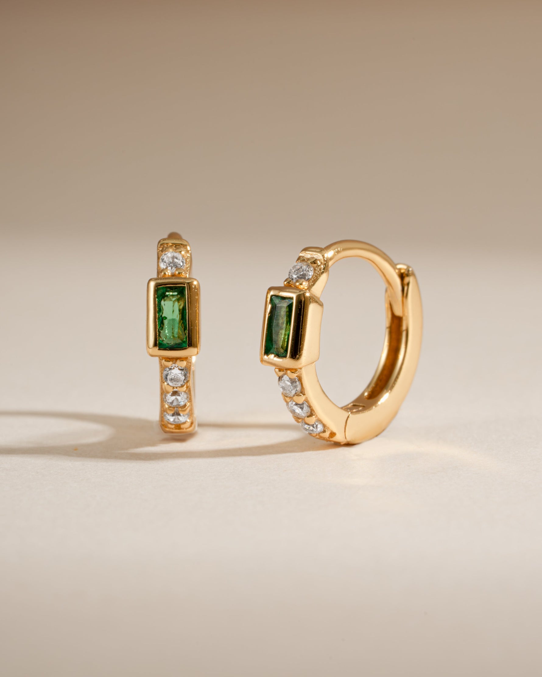 Gold Sami Jewels emerald baguette huggie earrings featuring sparkling emerald gemstones in a sleek hoop design.