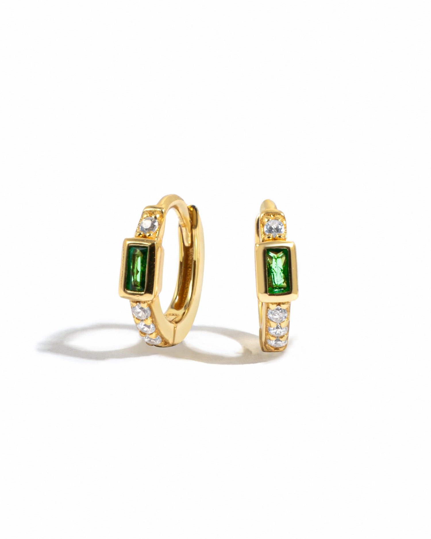Gold emerald baguette huggie earrings from Sami Jewels displayed on a white background.