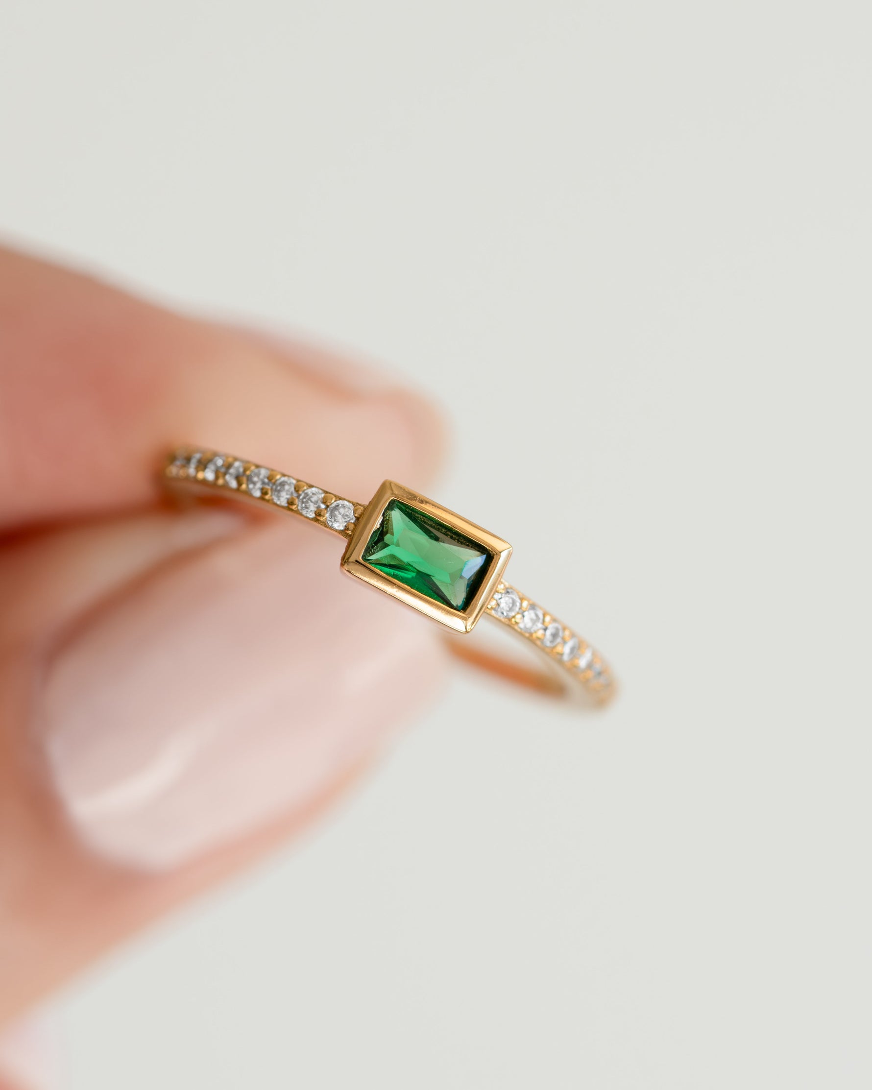 emerald baguette ring with pave band in gold held between fingers