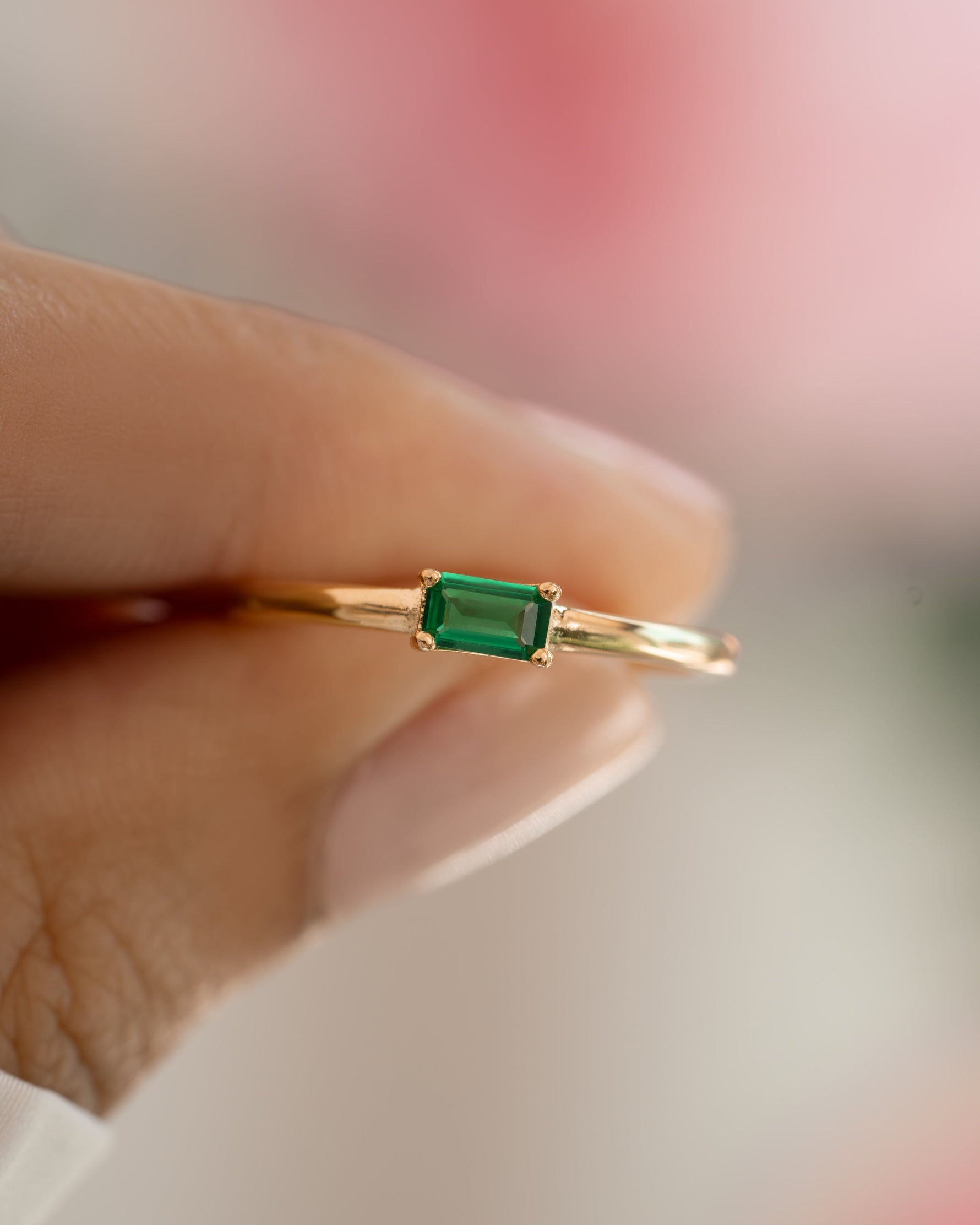 emerald baguette ring in gold held between two fingers