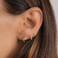 a close up of a model with three piercings, a small gold hoop earring with emerald gemstones in her first piercing, a small diamond huggie hoop in her second piercing, and a tiny diamond stud on her third piercing