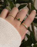 Gold stack of Sami Jewels emerald cushion ring with a vibrant green emerald gemstone on a model's finger.