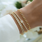 Gold Sami Jewels emerald-cut bezel tennis bracelet shown stacked with other bracelets on a model's wrist.