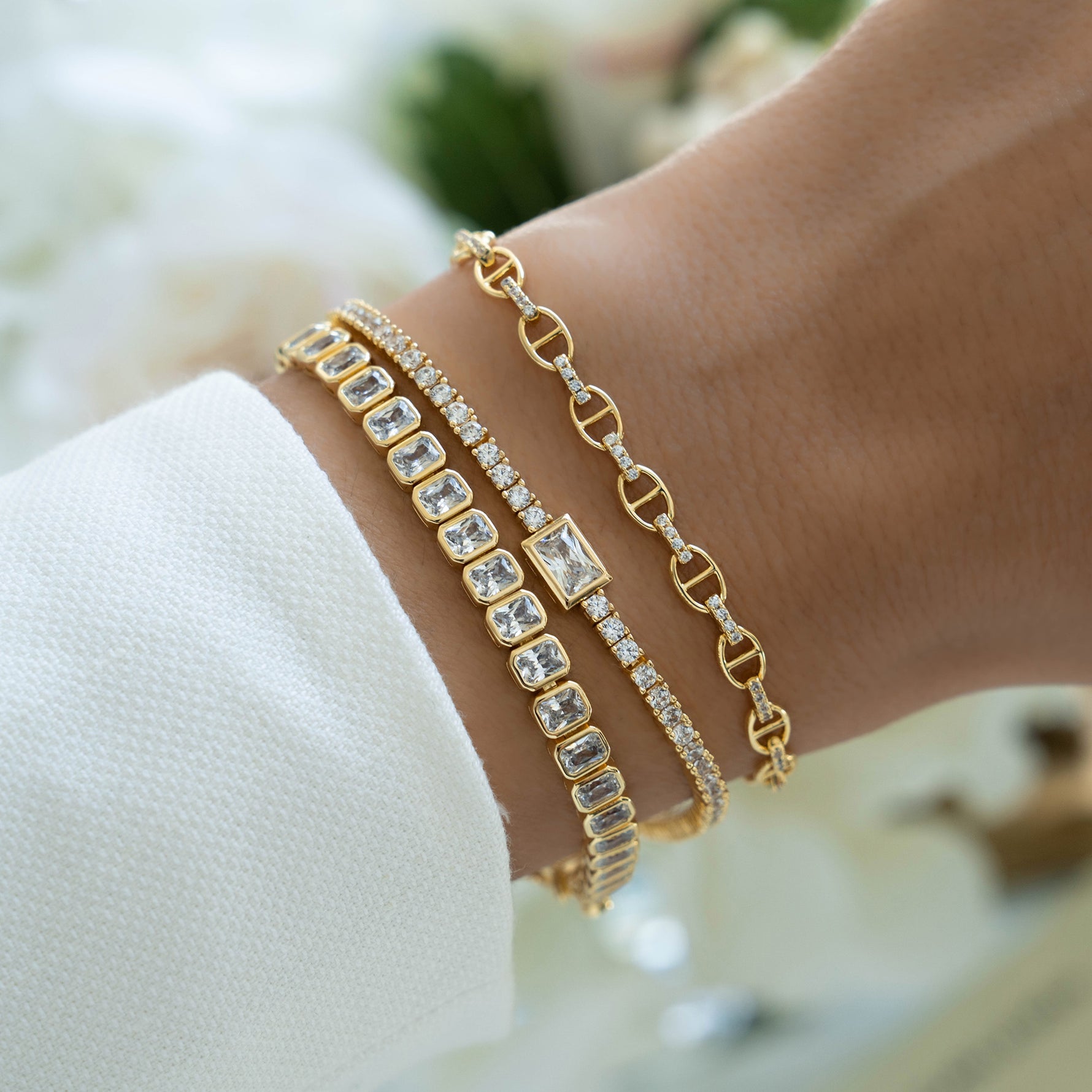 Gold Sami Jewels emerald-cut bezel tennis bracelet shown stacked with other bracelets on a model's wrist.