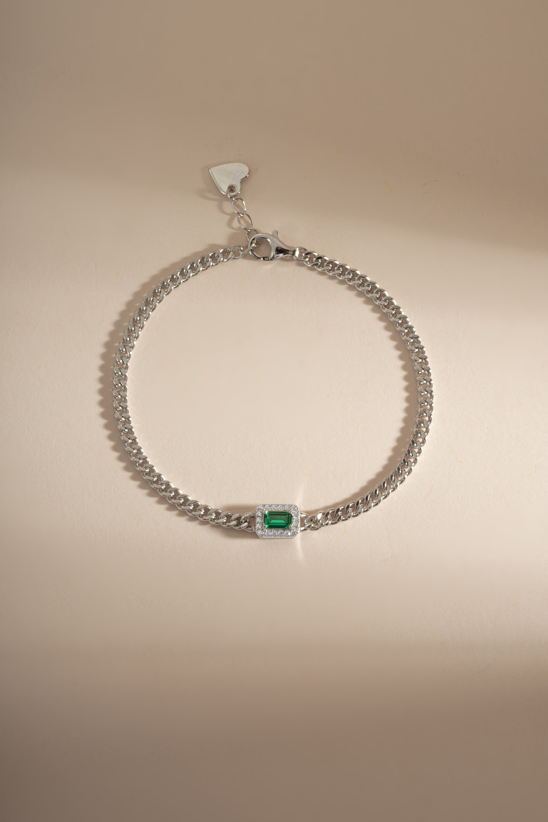 Emerald-cut emerald bracelet with diamond halo and silver setting, featuring intricate detailing and sparkling gemstones.