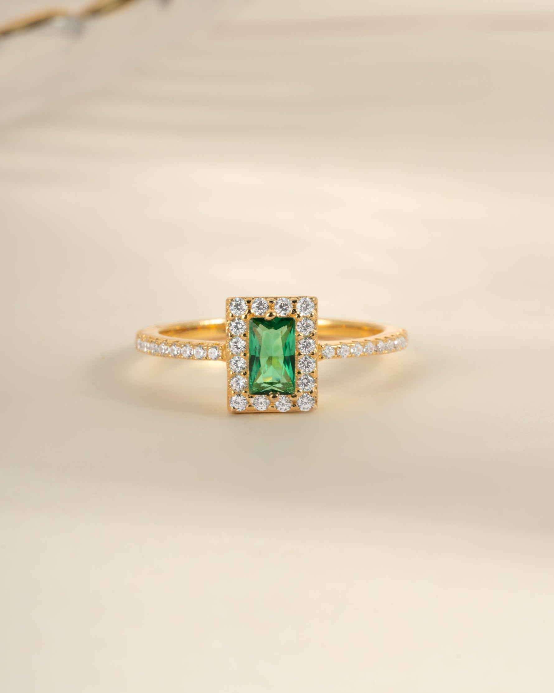 Sami Jewels emerald-cut emerald ring with gold band, showcasing a sparkling green gemstone from a front view.