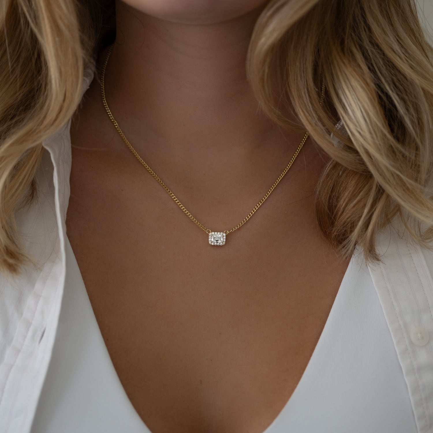 Model with blonde hair wearing halo emerald cut necklace on Cuban chain, adding a touch of elegance and shine