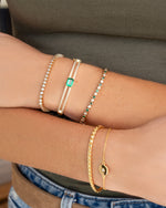 Gold Sami Jewels emerald pavé bangle bracelet with sparkling emerald and diamond accents, worn on a model's wrist.