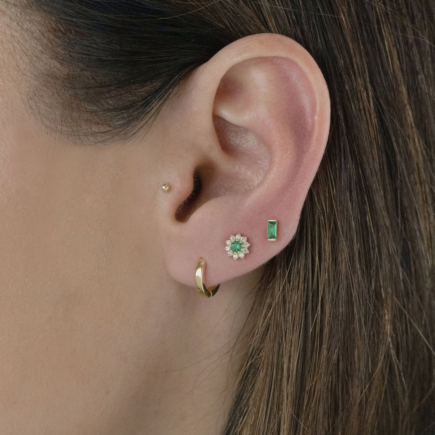 Gold emerald earrings in models ear.