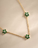 Close-up of SJ Faire emerald flower charm necklace with gold chain, showcasing intricate floral design and vibrant green gemstones.