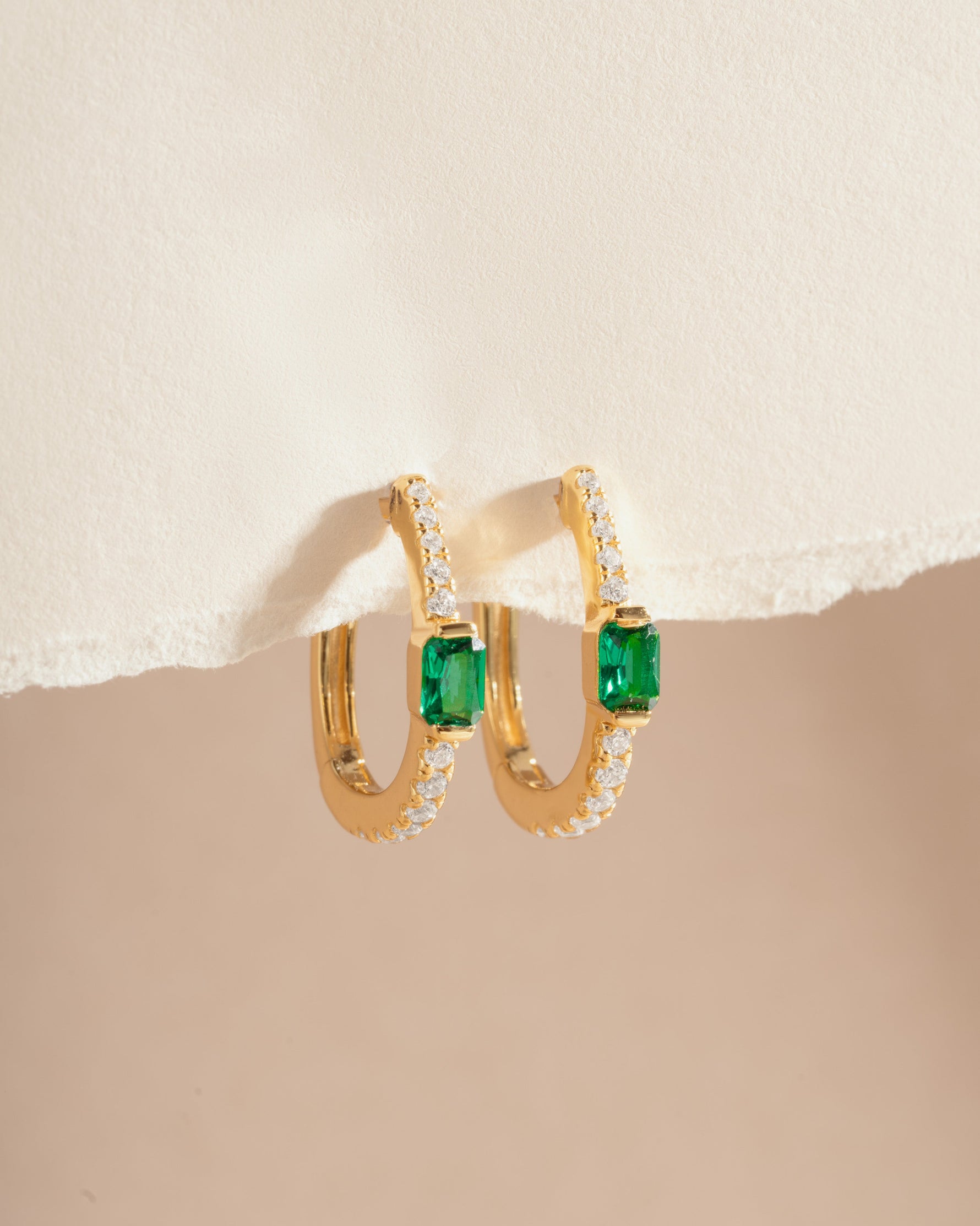 Close-up of gold emerald hoop earrings from Sami Jewels, showcasing vibrant green gemstones and elegant hoop design.
